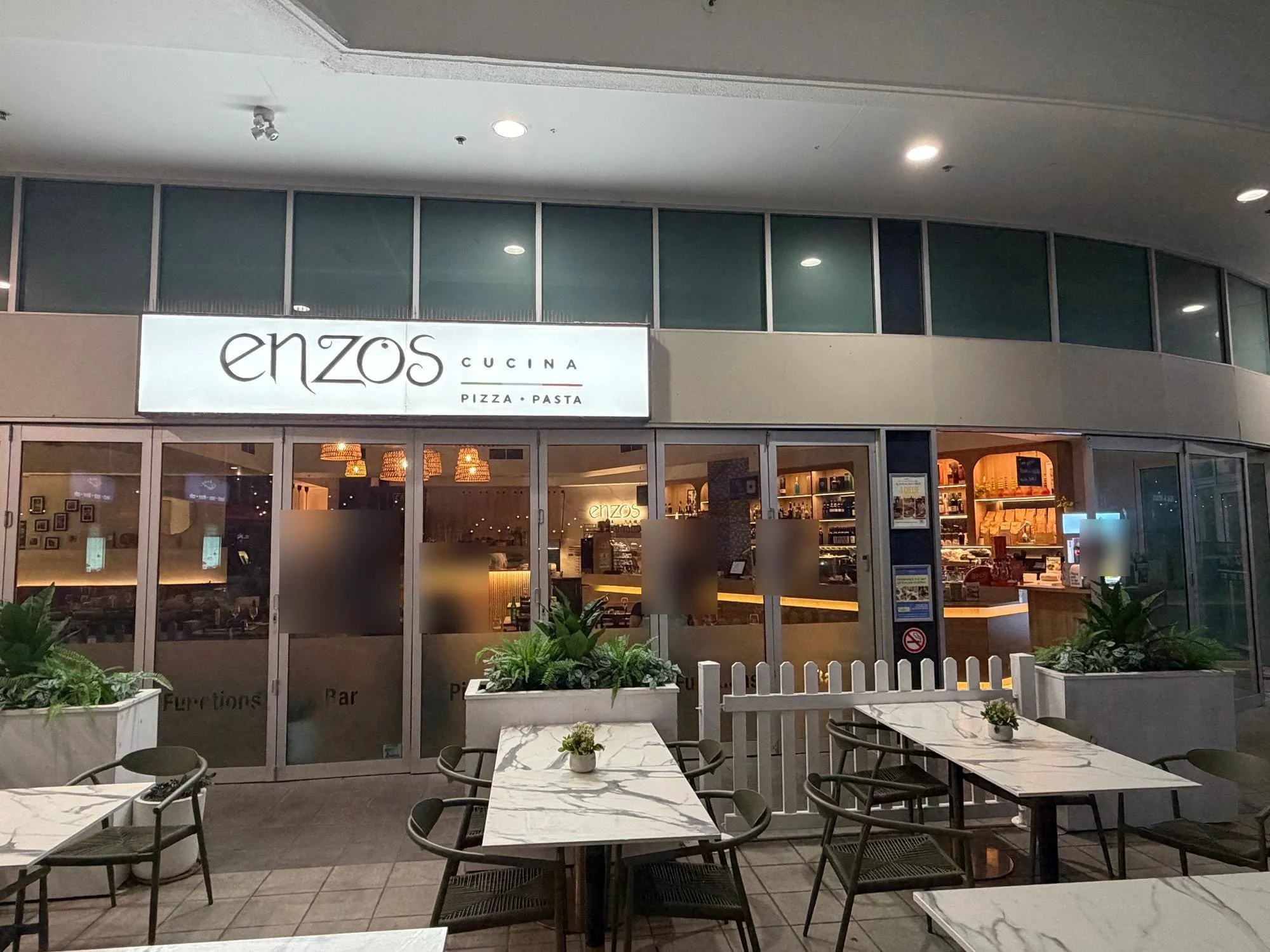 Enzos Cucina at Aqua, a white sign reading "enzos cucina, pizza pasta" above marble-topped tables set out in front.