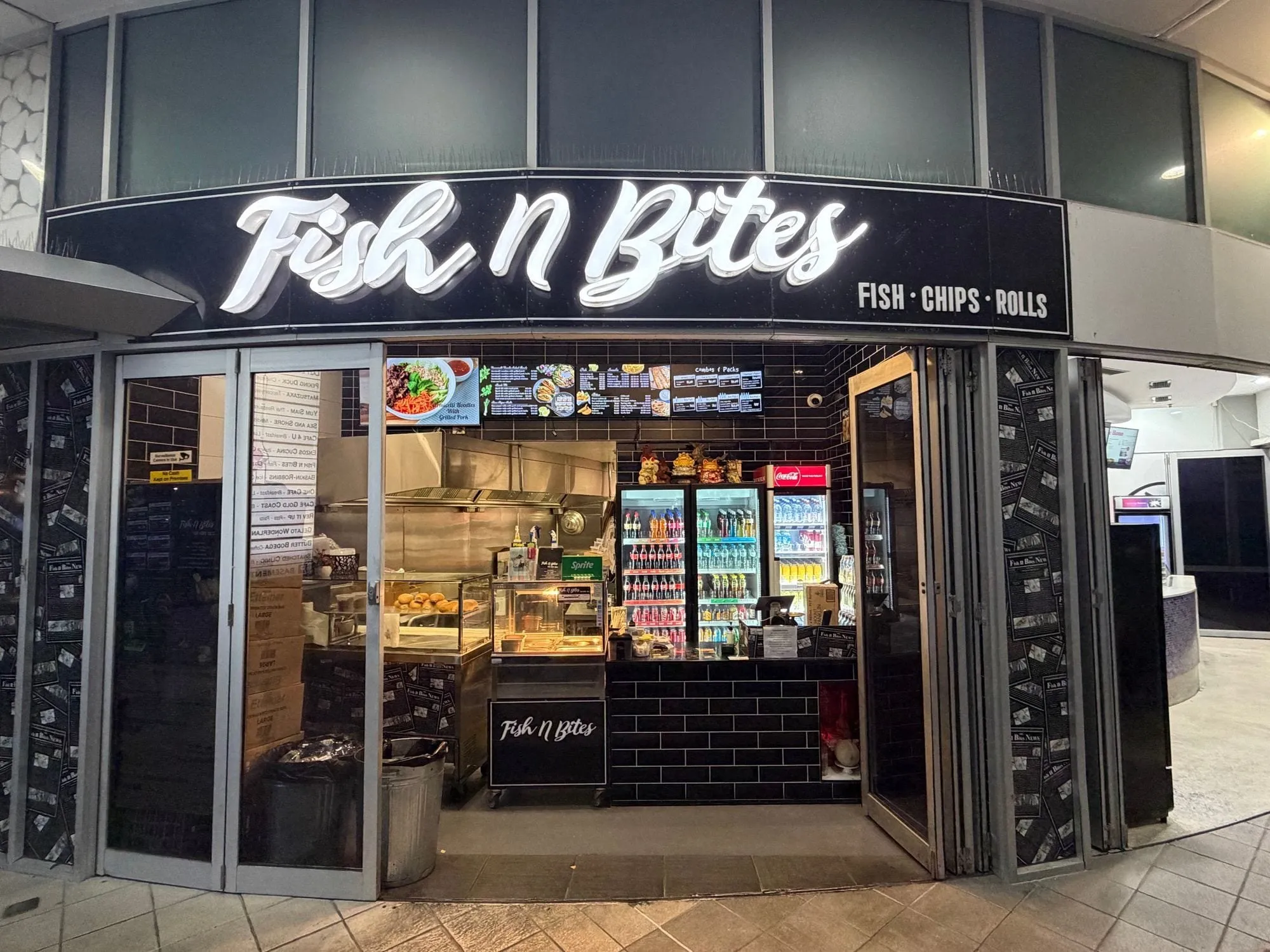 The Fish N Bites shopfront at Aqua, its curved black sign in white script above an open servery, reading fish, chips and rolls.