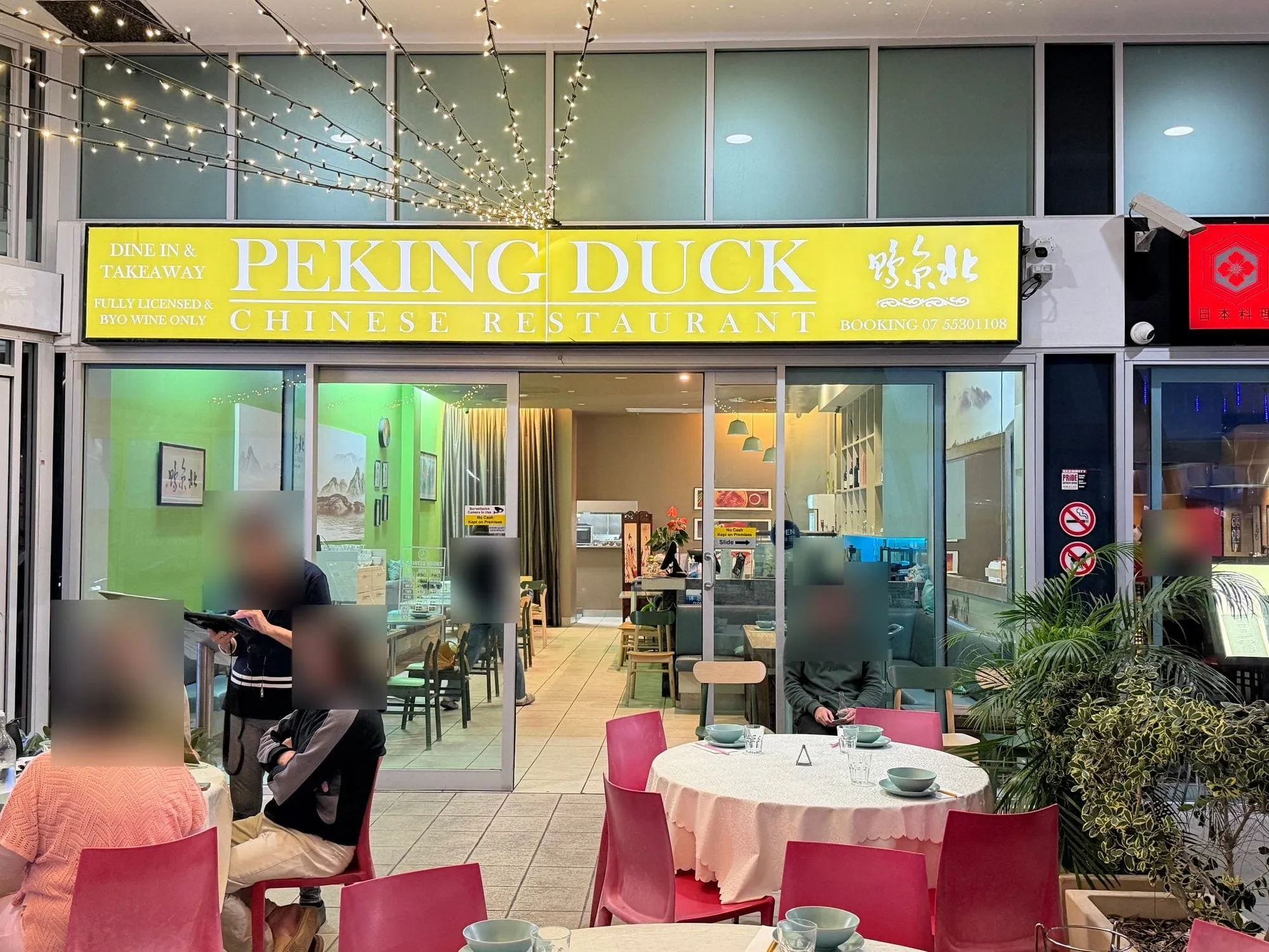 Peking Duck Chinese Restaurant at Aqua, a yellow sign above the entrance, with round tables and red chairs set for service inside.