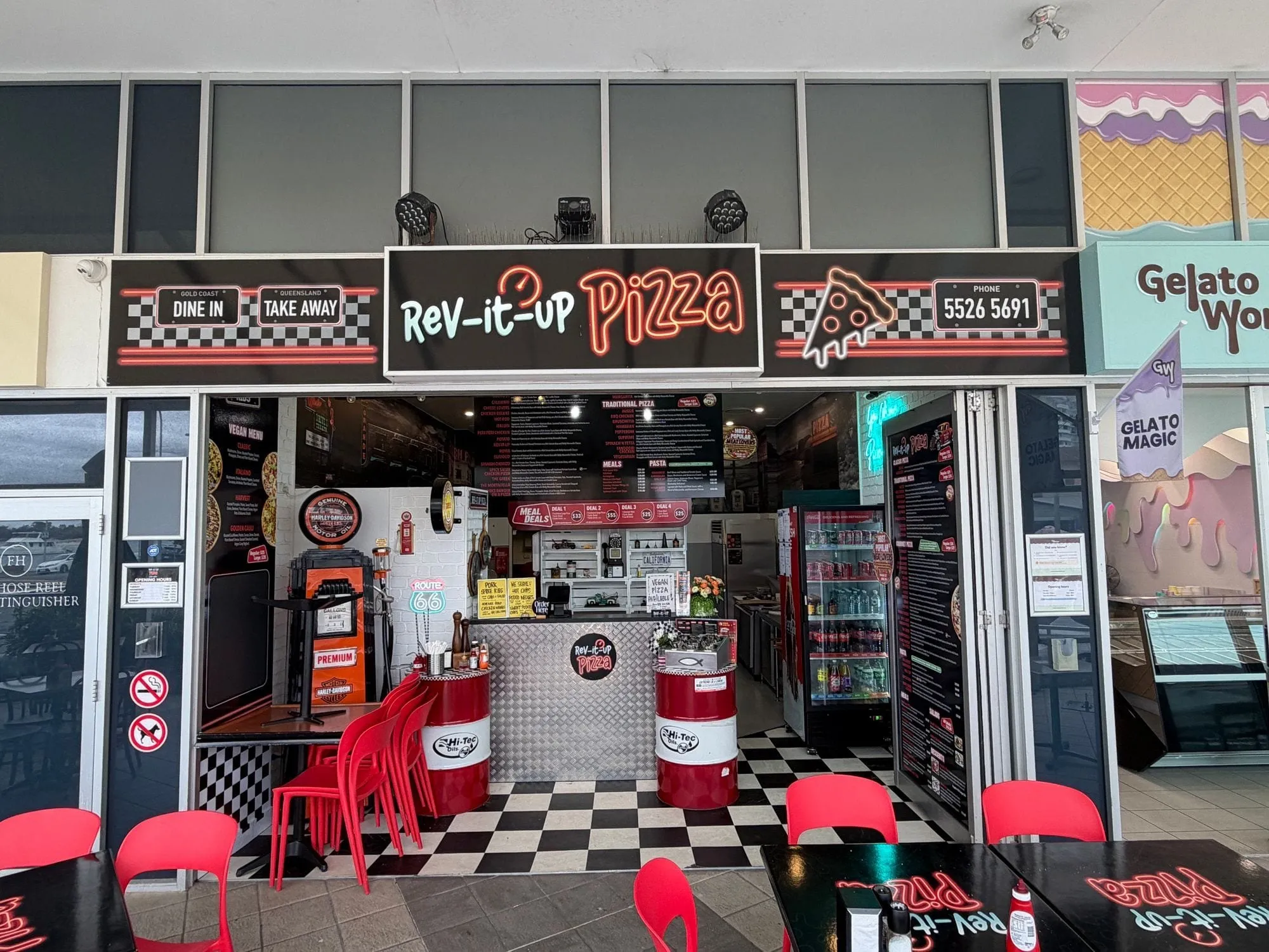 The Rev It Up Pizza shopfront at Aqua, its red-and-white sign reading "Dine in" and "Take away", with a black-and-white chequered floor and red stools inside.