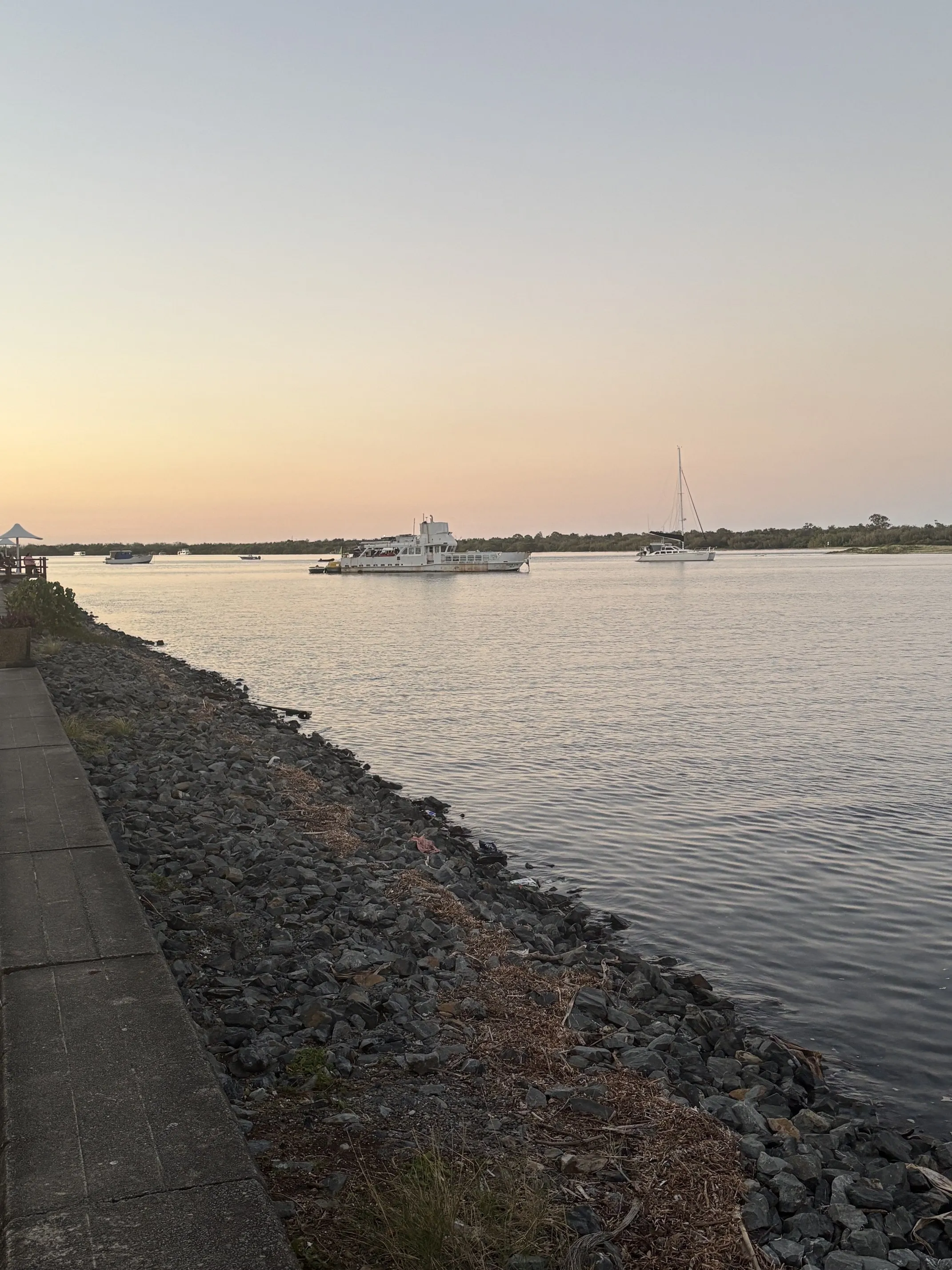 The rock-edged Labrador shoreline at sunset, with moored boats on the calm water of the Broadwater.